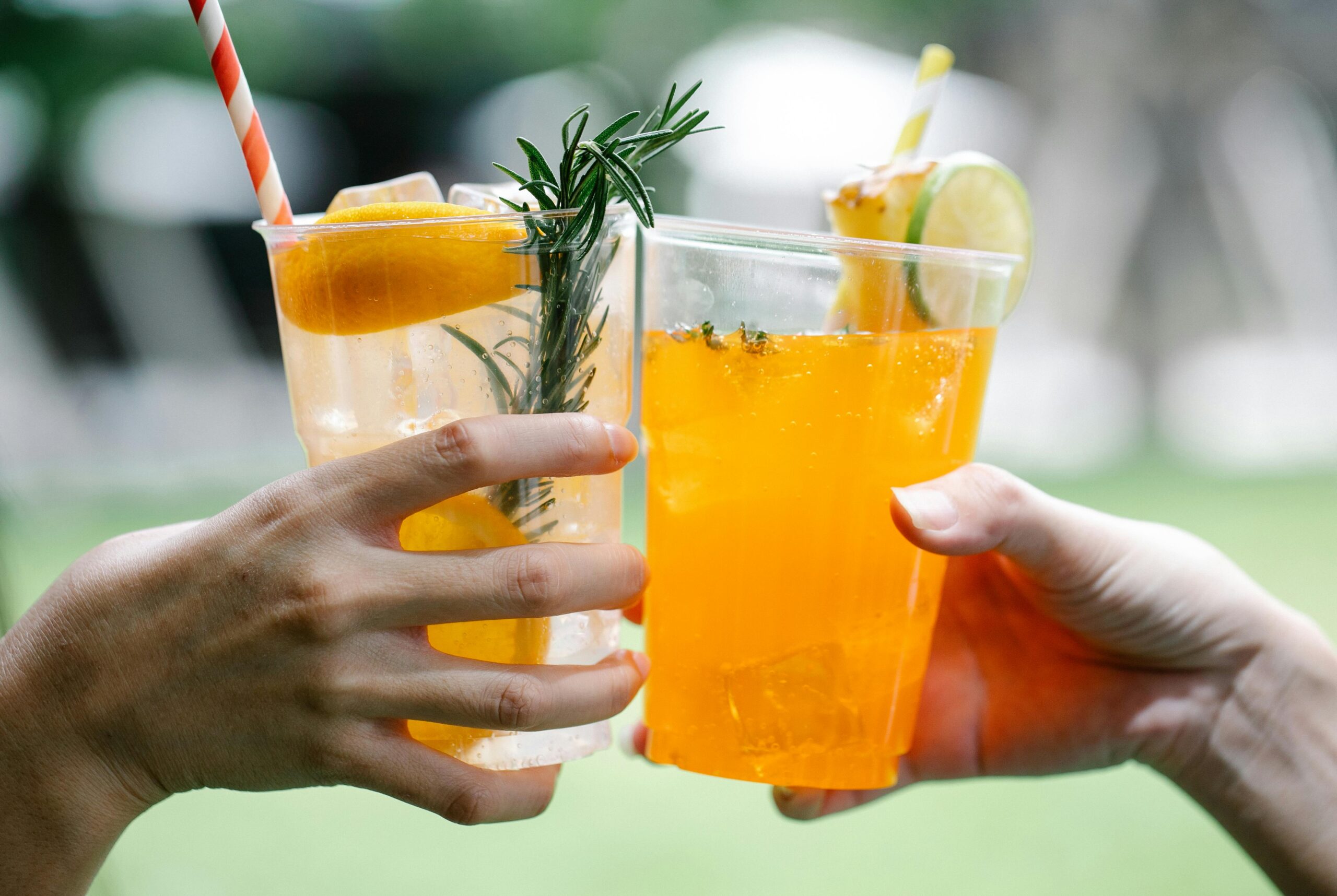 Close-up of hands toasting with citrus-infused drinks in outdoor setting.